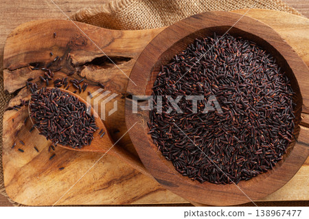 Natural black rice in a wooden bowl and spoon on a wooden surface in rustic style, top view Natural black rice in a wooden bowl and spoon on a wooden surface in rustic style, top view 138967477