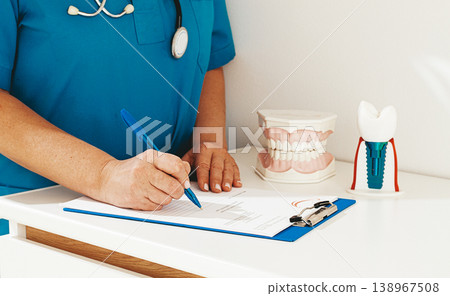 A dentist in a blue uniform studies patient information and prepares for treatment in a modern dental office 138967508