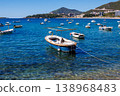 Small fishing boat anchored in crystal clear turquoise water near Adriatic coast with mountains and coastal town in background, sunny summer day, calm sea and travel vibe 138968483
