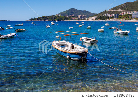 Small fishing boat anchored in crystal clear turquoise water near Adriatic coast with mountains and coastal town in background, sunny summer day, calm sea and travel vibe Small fishing boat anchored in crystal clear turquoise water near Adriatic coast with mountains and coastal town in background, sunny summer day, calm sea and travel vibe 138968483