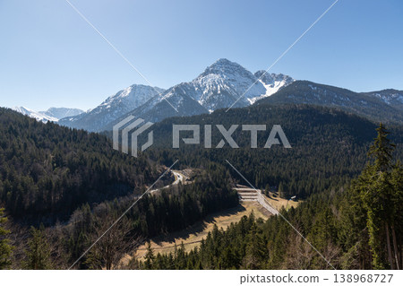 Snowcapped mountain above dense forest and winding road in Bavaria Germany Snowcapped mountain above dense forest and winding road in Bavaria Germany 138968727
