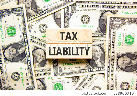 Tax liability words symbol. Concept words Tax liability on beautiful wooden blocks. Beautiful dollar bills background. Dollar bills. Business and Tax liability words concept. Copy space. 138969319