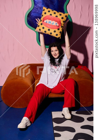 Woman holding decorative pillow confidently amid cozy studio setup Woman holding decorative pillow confidently amid cozy studio setup 138969998