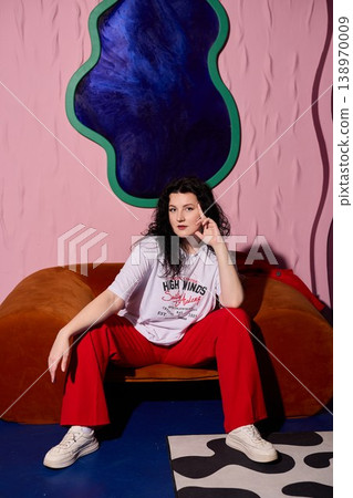Woman exhibiting happiness on vibrant orange couch with playful gestures Woman exhibiting happiness on vibrant orange couch with playful gestures 138970009