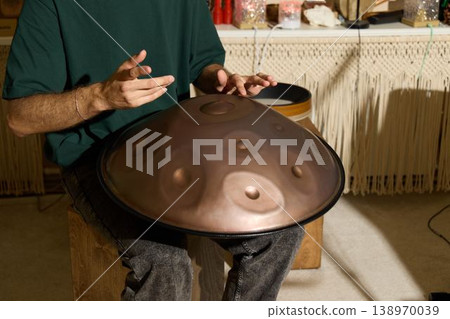 Focused hands gently striking handpan in warm studio environment Focused hands gently striking handpan in warm studio environment 138970039