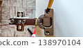 Marking the position of the screw hole on a furniture hinge with a pen 138970104