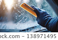 Hand in glove scraping frost from car windshield 138971495