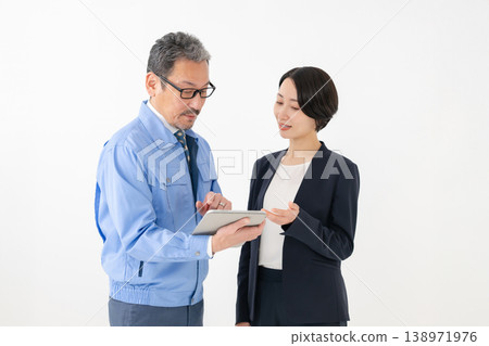 A man in work clothes holding a tablet and a businesswoman. A man in work clothes holding a tablet and a businesswoman. 138971976