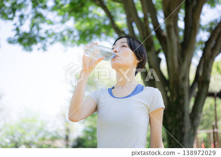 A profile portrait of a woman rehydrating outdoors amidst fresh greenery, during walking or running. A profile portrait of a woman rehydrating outdoors amidst fresh greenery, during walking or running. 138972029