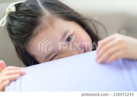 一個日本女孩躲在書包後面，在沙發上玩耍。 138972243
