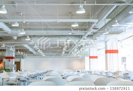 Empty white chair and table in shopping mall cafeteria with visible ceiling ventilation system, air ducts, pipes and fire sprinkler infrastructure, modern interior architecture. Public dining space. Empty white chair and table in shopping mall cafeteria with visible ceiling ventilation system, air ducts, pipes and fire sprinkler infrastructure, modern interior architecture. Public dining space. 138972911