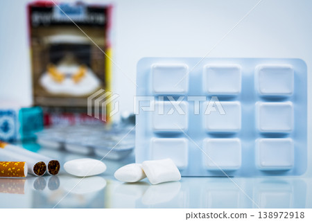 Nicotine chewing gum and blurred cigarette pack, healthcare concept. Smoking cessation therapy and addiction recovery, global awareness for world no tobacco day and public health improvement. Nicotine chewing gum and blurred cigarette pack, healthcare concept. Smoking cessation therapy and addiction recovery, global awareness for world no tobacco day and public health improvement. 138972918
