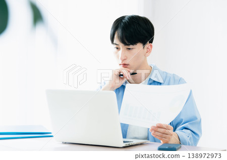 A young man thinking while looking at documents. A young man thinking while looking at documents. 138972973