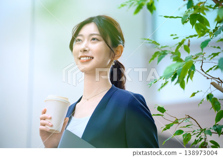 一位年輕的女商人笑容燦爛，手裡拿著一杯咖啡，坐在辦公室裡。 138973004