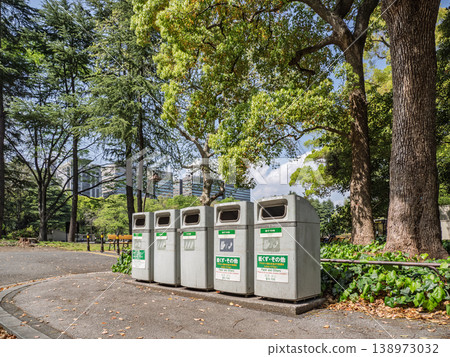 A view of sorting trash cans and park space in the distance; a landscape with multilingual signage. A view of sorting trash cans and park space in the distance; a landscape with multilingual signage. 138973032
