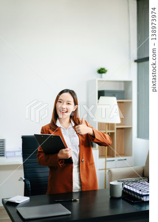 Asian female office worker business suits smiling at camera with working notepad, tablet and laptop documents in office 138973974