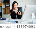 Asian businesswoman in brown blazer working on laptop, analyzing financial data with smartphone. at office 138974091