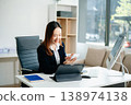 Asian female office worker business suits smiling at camera with working notepad, tablet and laptop documents in office 138974138