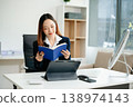 Asian female office worker business suits smiling at camera with working notepad, tablet and laptop documents in office 138974143