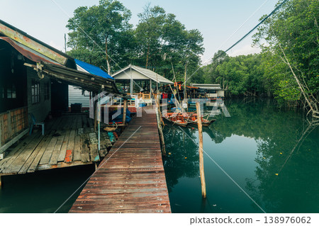 Traditional wooden boats and stilt houses along a calm canal surrounded by lush green mangrove forest. Traditional wooden boats and stilt houses along a calm canal surrounded by lush green mangrove forest. 138976062