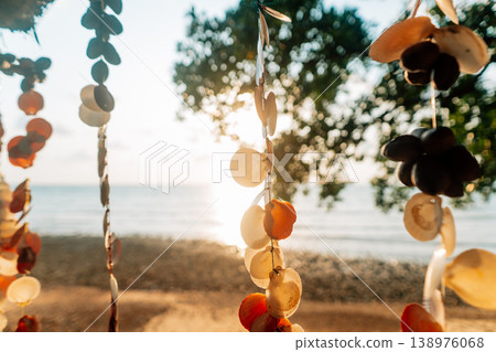 Close up of a decorative handmade seashell mobile hanging with a beautiful blurred tropical beach background at sunset. Close up of a decorative handmade seashell mobile hanging with a beautiful blurred tropical beach background at sunset. 138976068