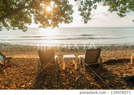 Relaxing Beach Chairs Under Tree Shade at Sunrise on a Pebbly Shore 138976071