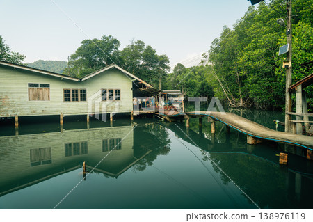 Traditional wooden boats and stilt houses along a calm canal surrounded by lush green mangrove forest. Traditional wooden boats and stilt houses along a calm canal surrounded by lush green mangrove forest. 138976119