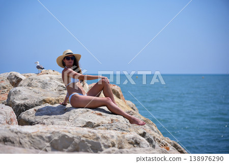 Woman enjoying sun on seaside rocks in bikini during summer day 138976290