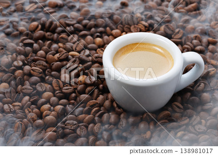 Espresso shot with creamy crema in white cup surrounded by aromatic roasted coffee beans and rising steam Espresso shot with creamy crema in white cup surrounded by aromatic roasted coffee beans and rising steam 138981017