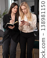 Two young professional businesswomen collaborating, having a discussion, and reviewing information on a smartphone and notebook during a meeting in a modern office environment 138981150