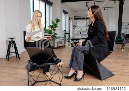 Professional women collaborating and exchanging ideas during a business meeting in a contemporary workspace, reviewing documents and taking notes to plan strategies Professional women collaborating and exchanging ideas during a business meeting in a contemporary workspace, reviewing documents and taking notes to plan strategies 138981152