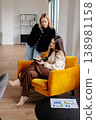 Two businesswomen discussing new project ideas, one writing notes in a planner while the other stands over, engaging in a productive teamwork session in a contemporary office space 138981158