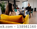 Two women engaging in a professional business meeting, one taking notes while the other uses a laptop, fostering discussion and collaboration in a contemporary coworking space 138981160