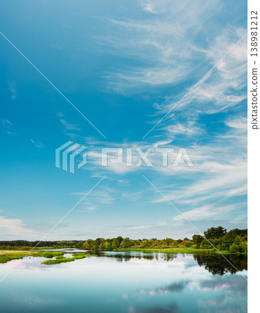 Peaceful river reflecting cirrus clouds under a vibrant blue sky Peaceful river reflecting cirrus clouds under a vibrant blue sky 138981212