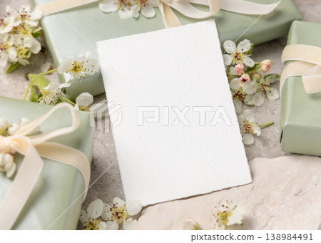 Blank card mockup with white spring flowers and gift boxes on beige stone. Wedding invitation Blank card mockup with white spring flowers and gift boxes on beige stone. Wedding invitation 138984491