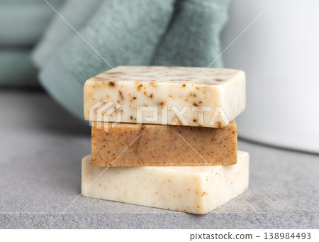 Brown and beige handmade solid soap bars near light green bath towel. Exfoliating scrub soap set 138984493