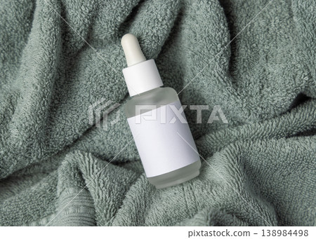 Glass dropper bottle with blank label mockup on sage green bath towel, unbranded cosmetic packaging 138984498