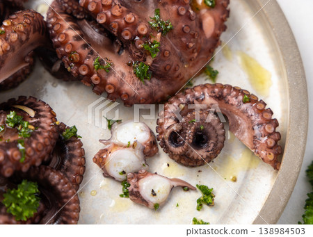 Boiled octopus tentacles and sliced pieces on ceramic plate top view. Olive oil and parsley dressing Boiled octopus tentacles and sliced pieces on ceramic plate top view. Olive oil and parsley dressing 138984503