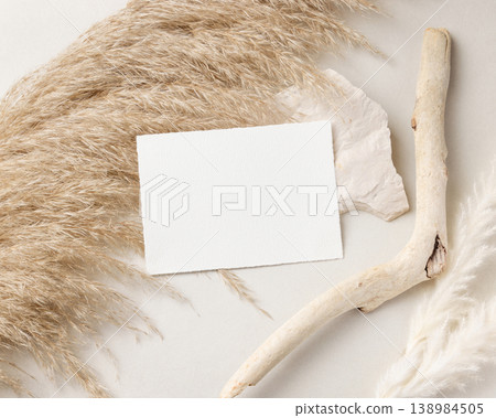 Blank card mockup on beige stone with driftwood and pampas grass top view, boho wedding stationery 138984505