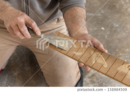 Construction worker applying adhesive on parquet planks during flooring installation in apartment 138984509