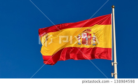 Spanish Flag Waving on Flagpole Against Clear Blue Sky, National Symbol of Spain Spanish Flag Waving on Flagpole Against Clear Blue Sky, National Symbol of Spain 138984598
