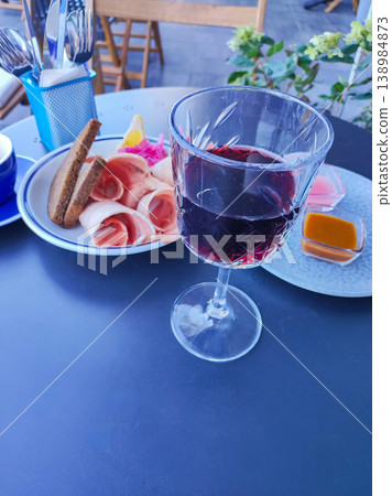Glass of red wine and meat appetizer on a table in an outdoor terrace cafe Glass of red wine and meat appetizer on a table in an outdoor terrace cafe 138984873