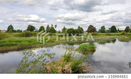 Peaceful summer landscape with a calm river flowing through a green countryside village Peaceful summer landscape with a calm river flowing through a green countryside village 138984881
