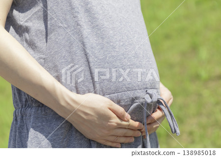 The image is of a pregnant woman touching her belly on a sunny day. The image is of a pregnant woman touching her belly on a sunny day. 138985018