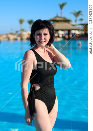 A striking woman in a black bikini stands knee-deep in a pool A striking woman in a black bikini stands knee-deep in a pool 138985105