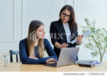 Confident female mentor teacher advising teaching young woman university student Confident female mentor teacher advising teaching young woman university student 138985320