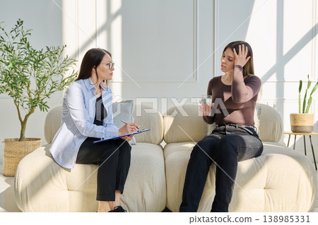 Sad upset young woman patient in therapy session in psychologist office Sad upset young woman patient in therapy session in psychologist office 138985331