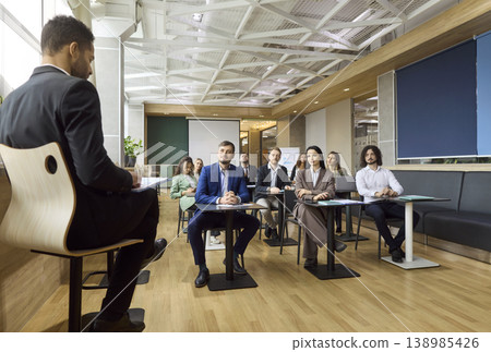 Business team listening to speaker during seminar presentation in modern office Business team listening to speaker during seminar presentation in modern office 138985426