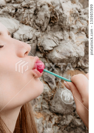 Lollipop woman portrait Woman enjoys tasting a pink candy sweet in front of a natural stone wall Lollipop woman portrait Woman enjoys tasting a pink candy sweet in front of a natural stone wall 138985999