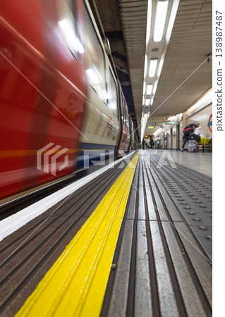 Blurred red train speeding past a yellow safety line on a platform 138987487